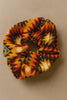 Afrocentric scrunchie with yellow, red, black geometric tribal pattern on neutral background
