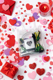 Valentine's themed flat lay with clear bag holding Afrocentric fabric bow headband, surrounded by red hearts, candle, and a gift box.