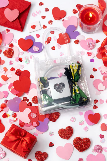 Valentine's themed flat lay with clear bag holding Afrocentric fabric bow headband, surrounded by red hearts, candle, and a gift box.