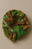 Afrocentric scrunchie with green, gold, and brown patterned fabric on neutral background