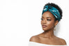 Woman wearing blue Afrocentric headwrap and gold hoop earrings against white background