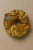 Handcrafted Afrocentric scrunchie with yellow, brown, and gold geometric patterns on beige background