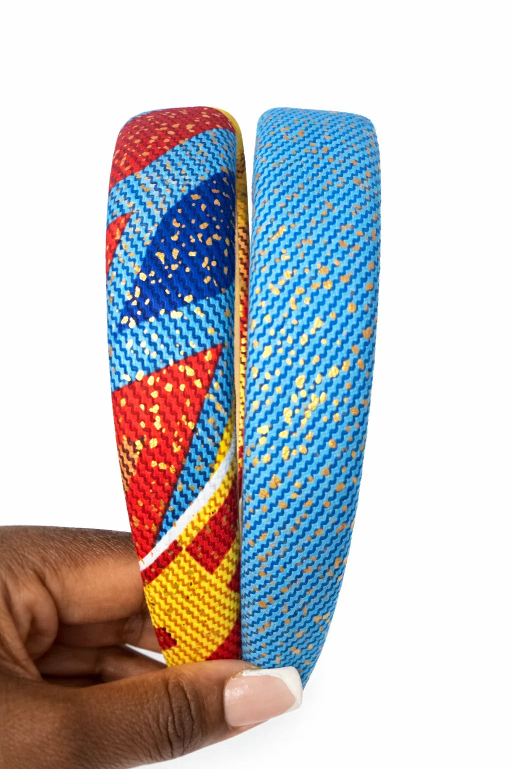 Hand holding two Afrocentric headbands with vibrant blue, red, yellow, and gold patterns