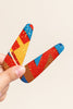 Hand holding two Afrocentric hair clips with vibrant red, yellow, and blue geometric patterns