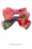 Two handcrafted Afrocentric hair bows with vibrant pink, gold, and blue patterns on white background.