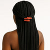 Woman with long box braids adorned with bright orange hair clips, shown from behind