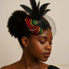 Woman wearing colorful Afrocentric fascinator hat with black feathers and mesh veil