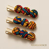Three gold hair clips with round, Afrocentric fabric-covered buttons in vibrant geometric patterns.