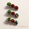 Three silver hair clips with colorful Afrocentric fabric patterns on a beige background.